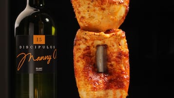 A skewer with grilled food and a bottle of wine on a table.