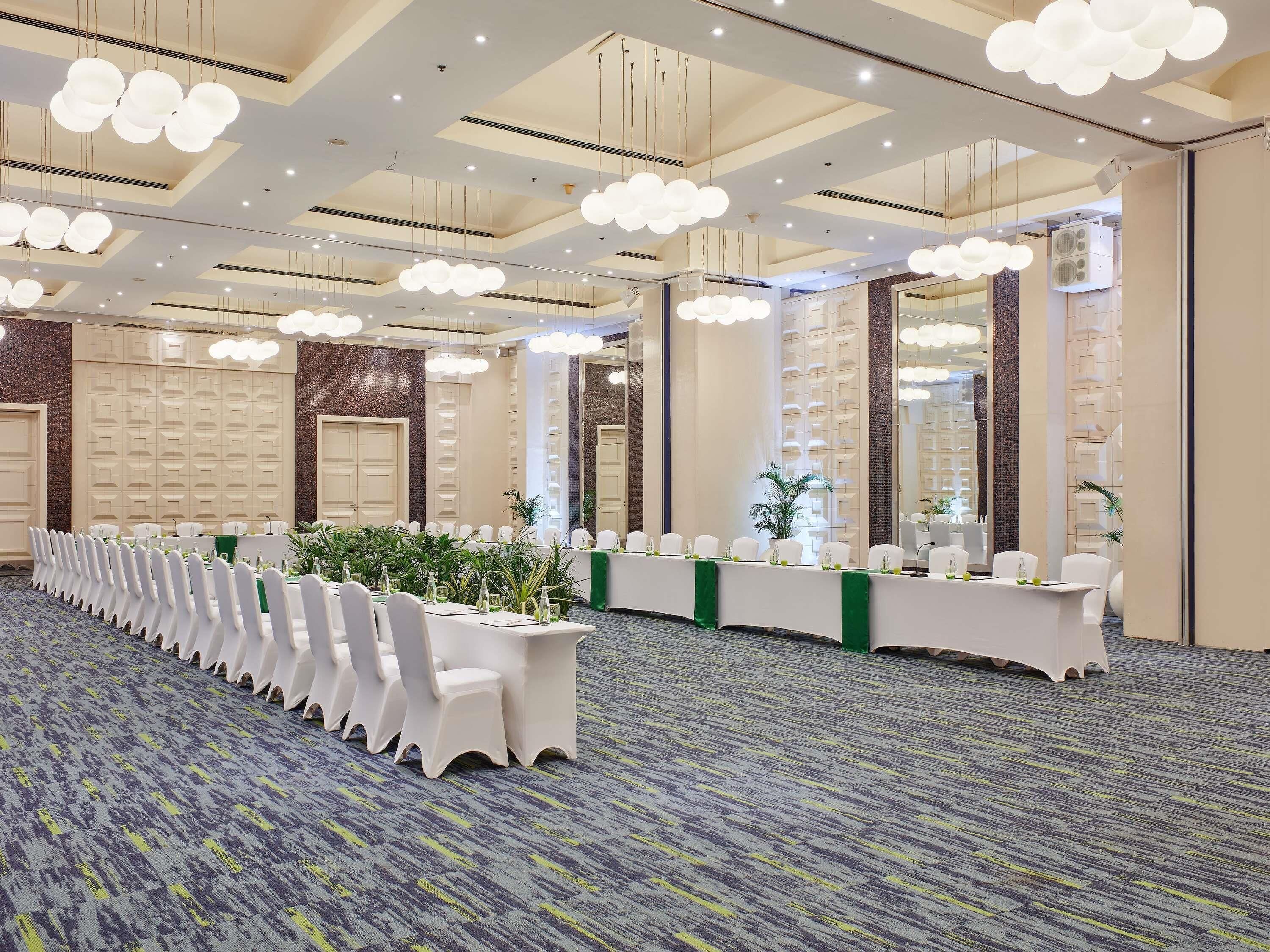 Un salón de conferencias con una larga mesa, sillas blancas e iluminación del techo.