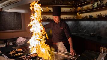 Un chef realiza un flambé con una llama grande sobre una mesa.
