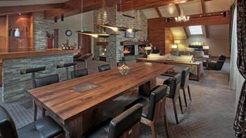 A spacious living area with a large wooden dining table, multiple chairs, a stone fireplace, and a cozy seating area with a sofa and armchairs.