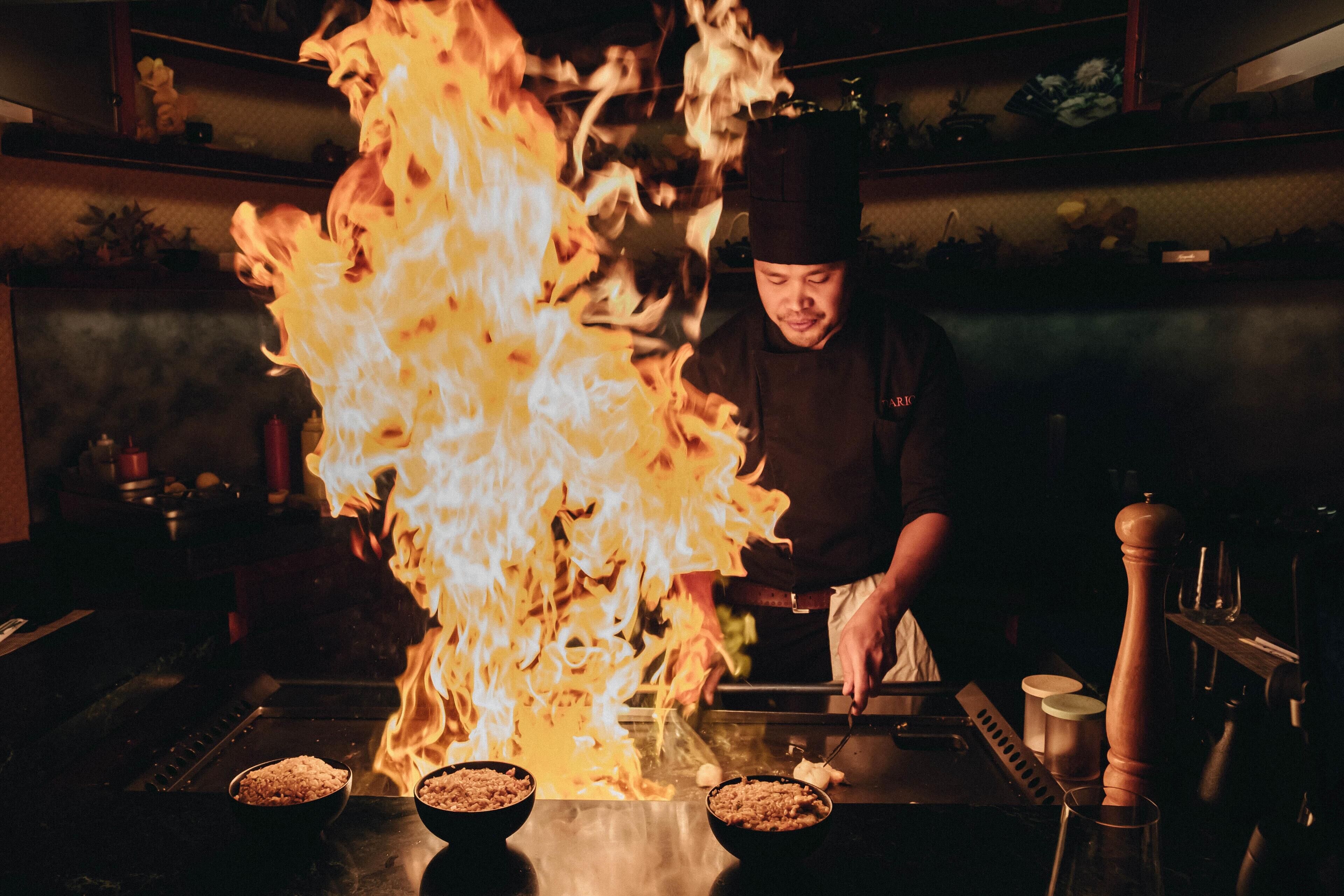 A chef cooking with flames on a grill.