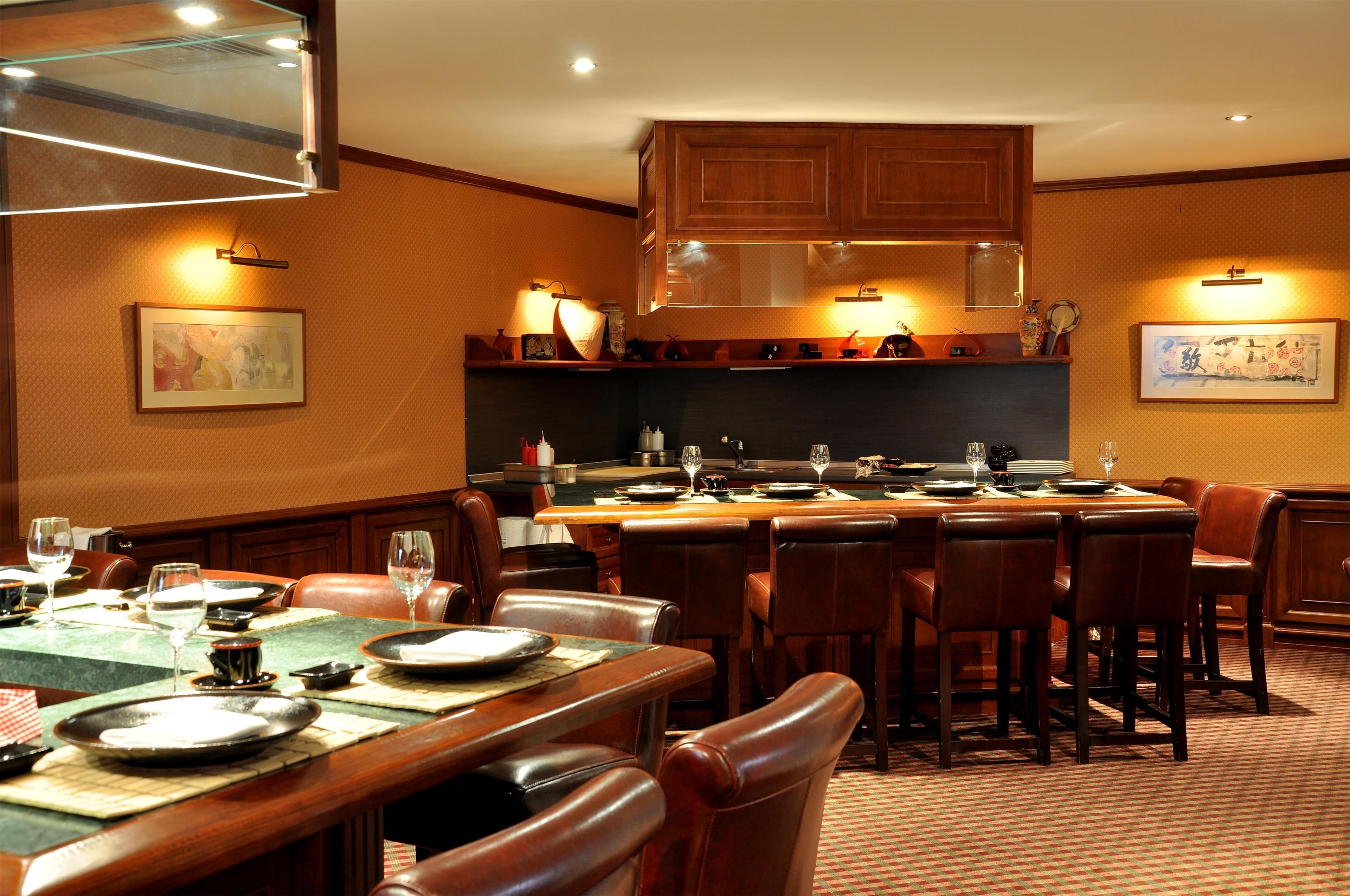 A restaurant with a long counter, multiple dining tables, and chairs. There are framed pictures on the walls.