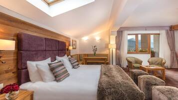 Habitación de hotel con una cama grande, cabecera de madera, tragaluz, zona de estar con sillas y vistas al exterior.