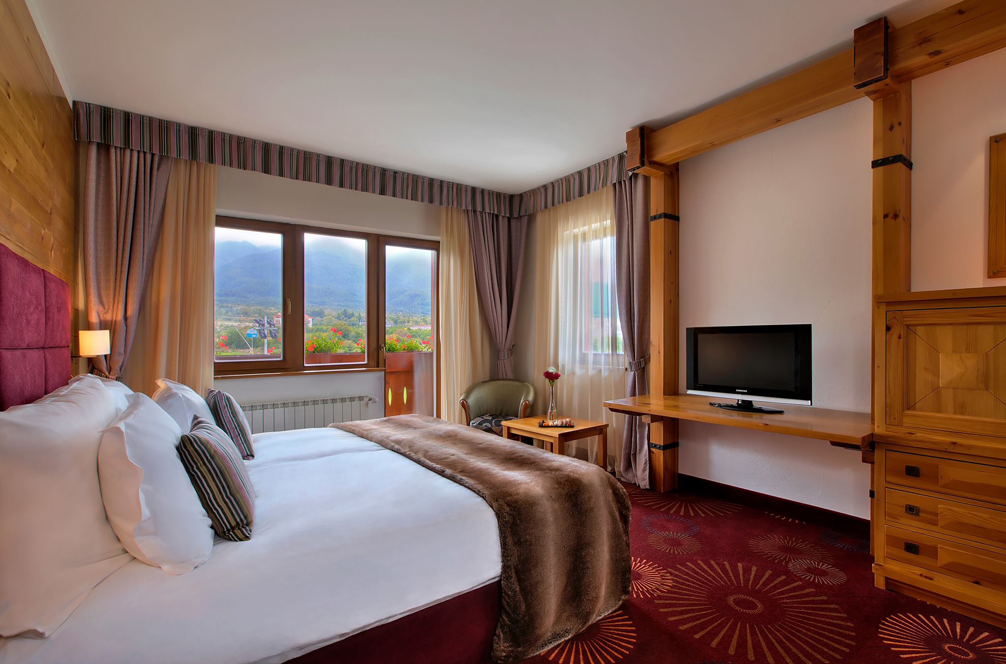 A hotel room with a large bed, a television, a desk, and a view of the mountains.