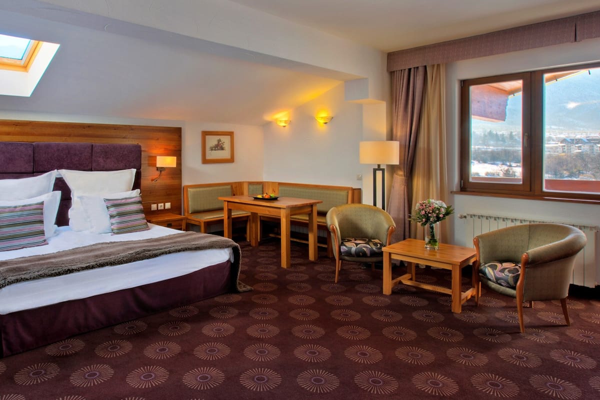 A hotel room with a bed, a desk, a chair, a lamp, a window, and a skylight.
