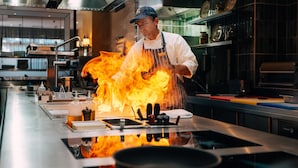 A chef cooking with flames on a stove in a modern kitchen. - Kempinski Hotel Grand Arena (Bansko)