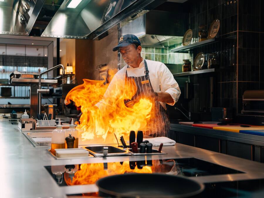 A chef cooking with flames on a stove in a modern kitchen.