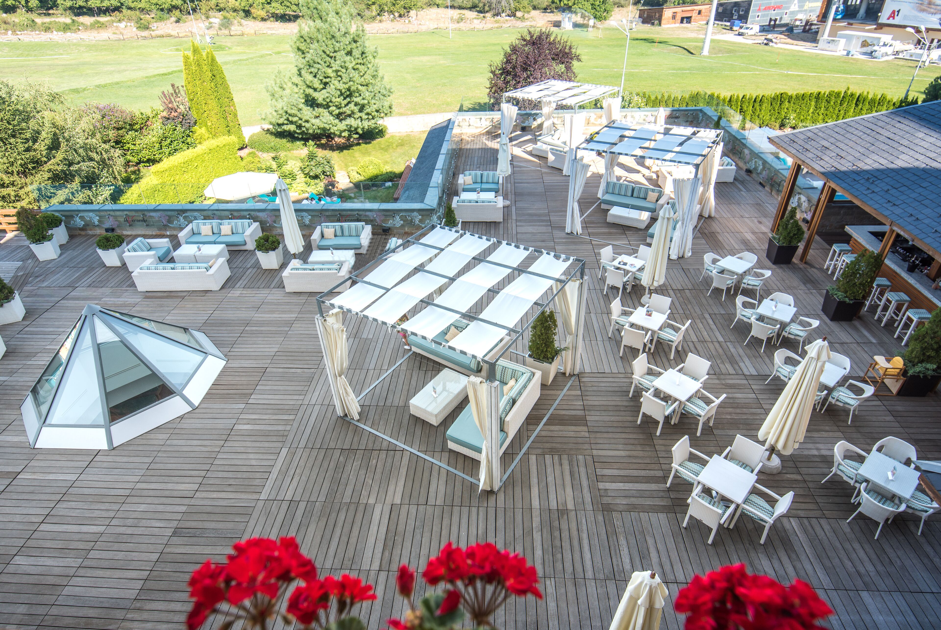 Un área de terraza en la azotea con varios conjuntos de mobiliario, incluyendo mesas y sillas, y un espacio lounge con paredes de vidrio.