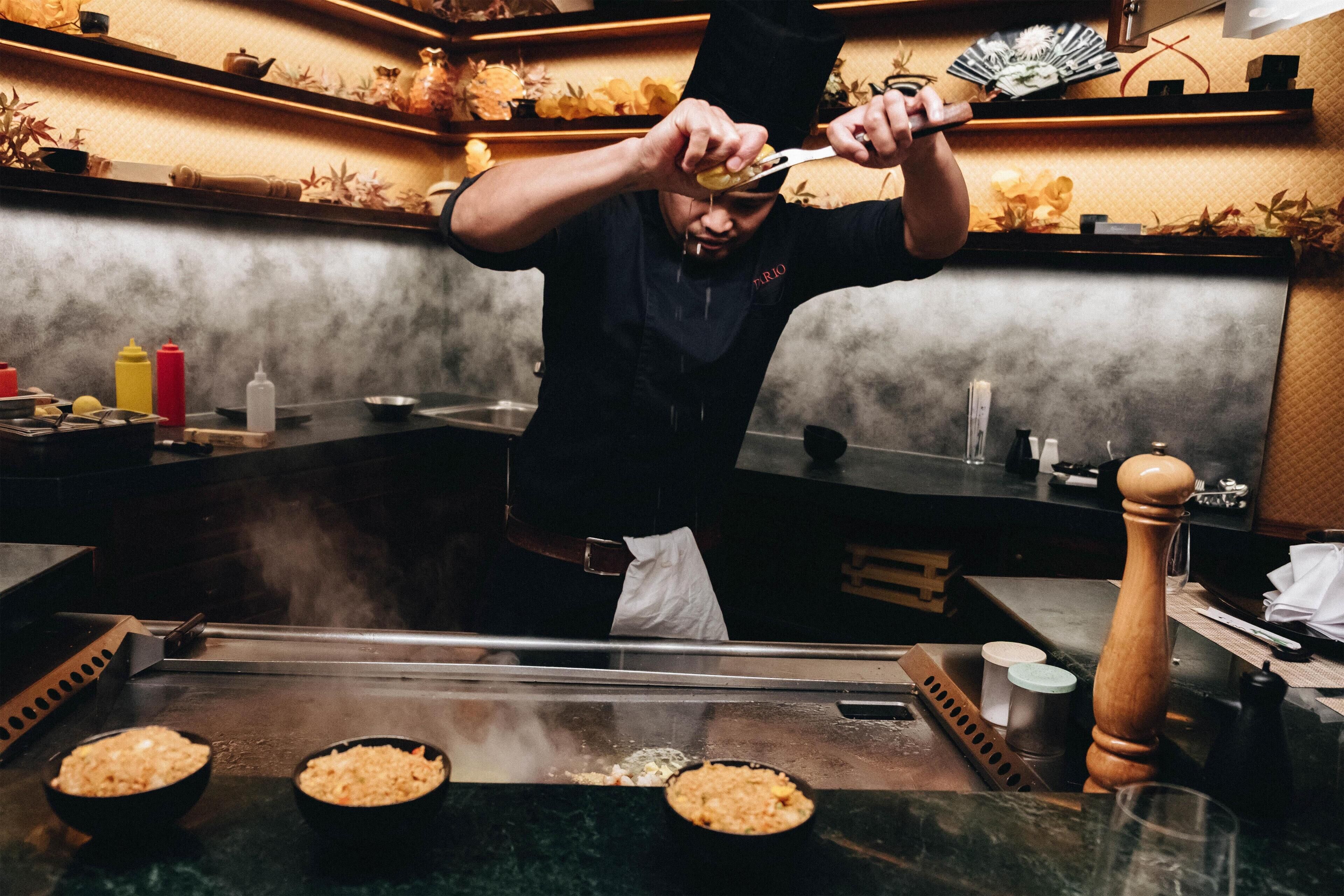 Un chef preparando comida en una parrilla dentro de una cocina con encimera de mármol y diferentes utensilios de cocina.