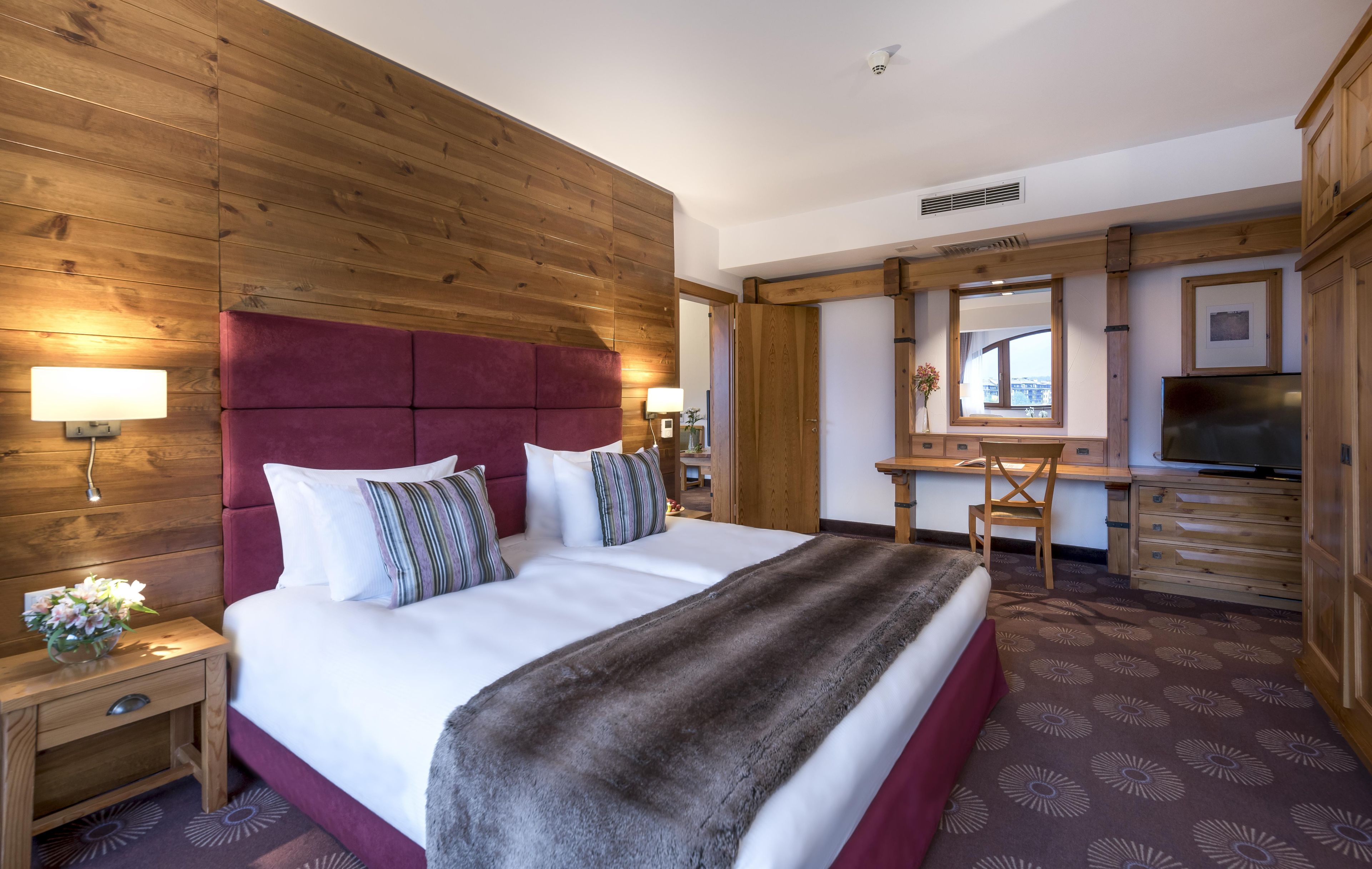 Habitación de hotel con una cama grande, cabecera de madera, un escritorio con una silla, un espejo y un televisor.