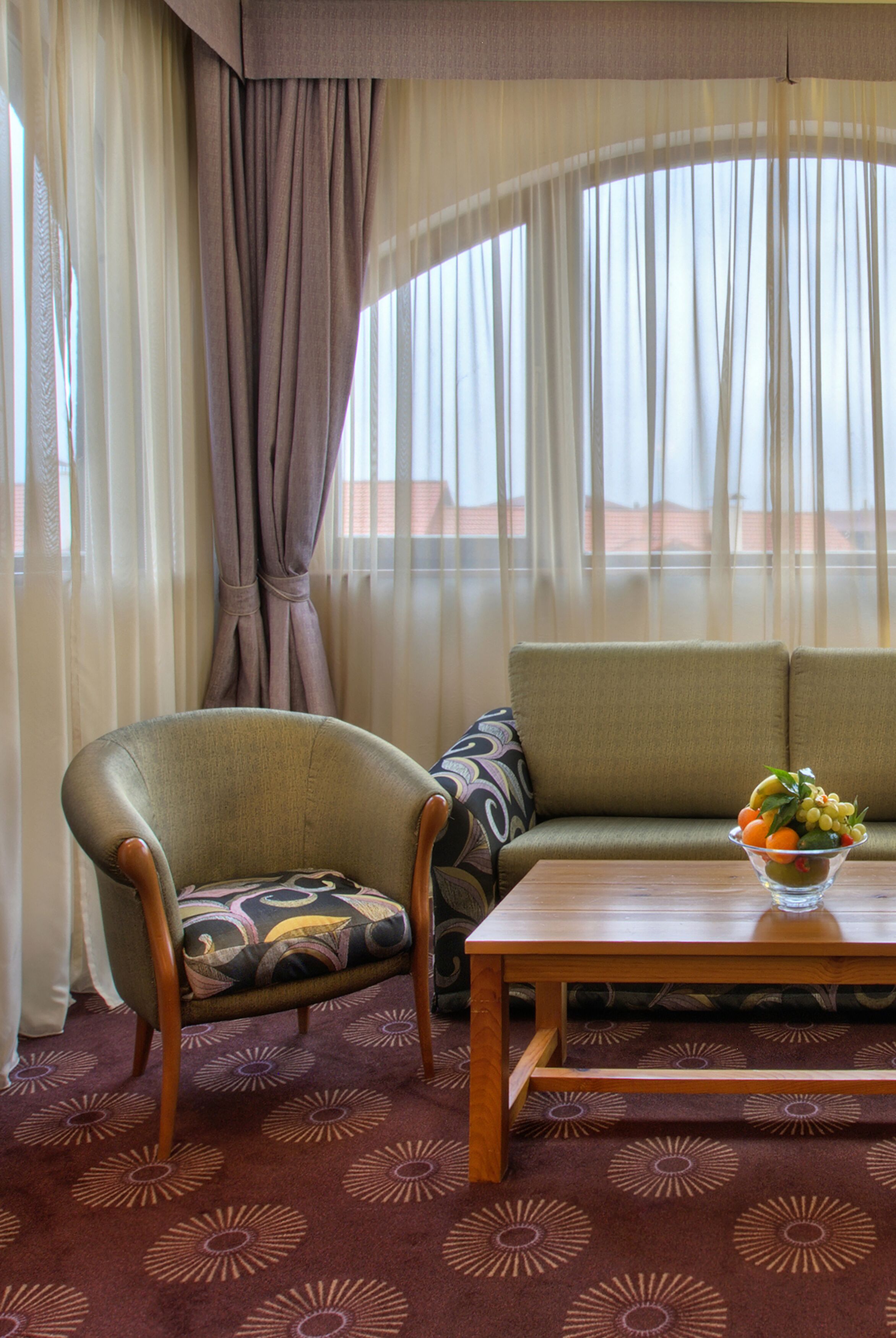 A room with a sofa, armchair, and a table with a fruit bowl.