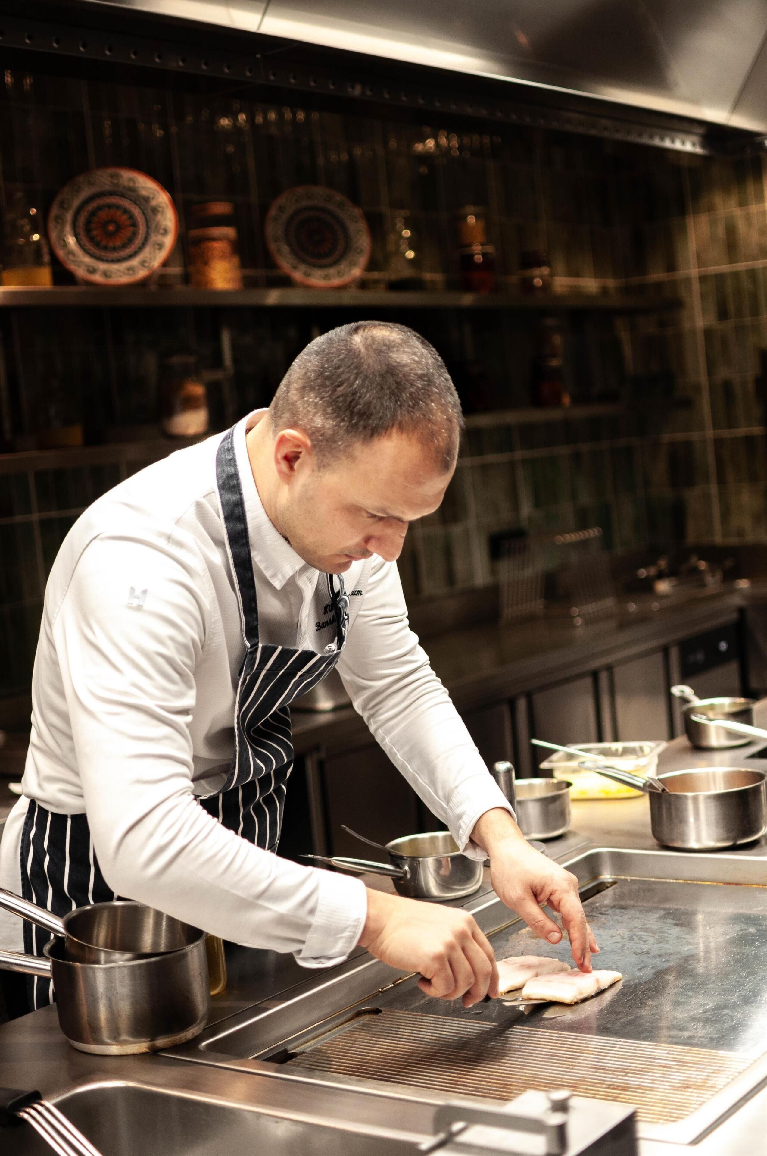 A chef preparing food on a grill in a kitchen.