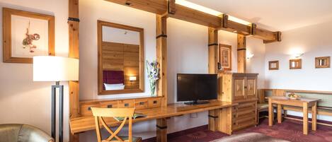 A wooden-framed room with a desk, chair, TV, and a small table with a plate of fruit.