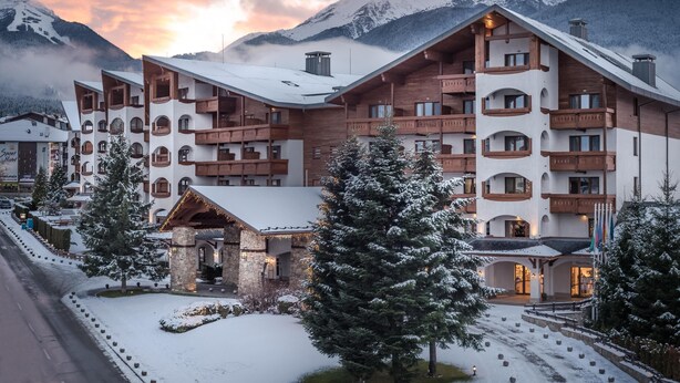 A multi-story hotel with wooden balconies and a stone facade, set against a backdrop of snow-covered mountains. - Kempinski Hotel Grand Arena (Bansko)