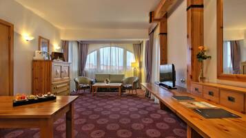 Una camera d'albergo con una scrivania in legno, televisore, divano e tavolo da pranzo.