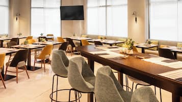 Un salón de conferencias con varias mesas y sillas, ventanas amplias y un televisor de pantalla plana en la pared.