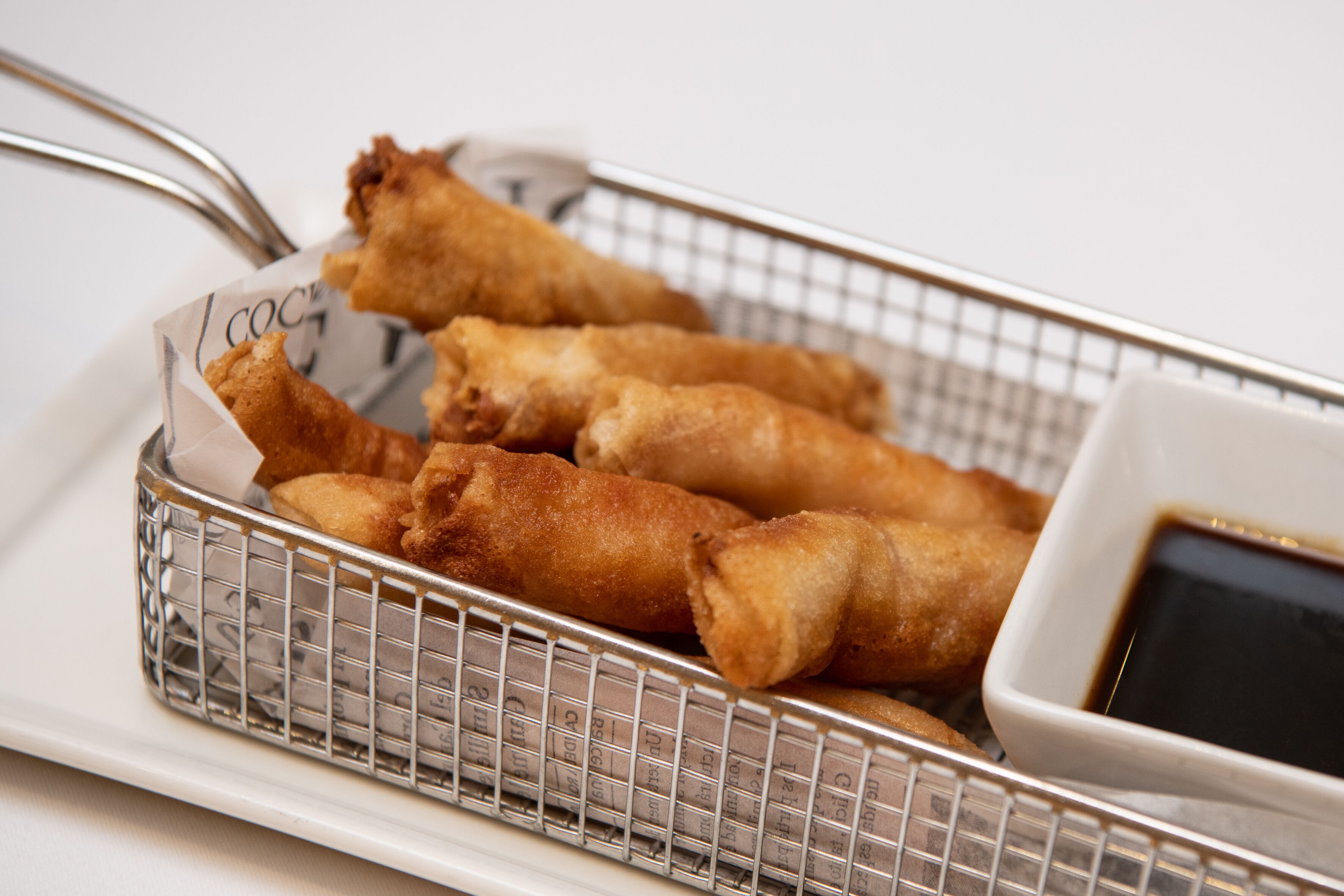 Una cesta de rollitos primavera fritos con salsa para mojar.