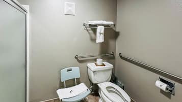 A small, single-occupancy bathroom with a toilet, a chair, a towel rack, and a handrail.