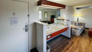 A hotel bathroom with a double sink, a mirror, a towel rack, and a trash can.