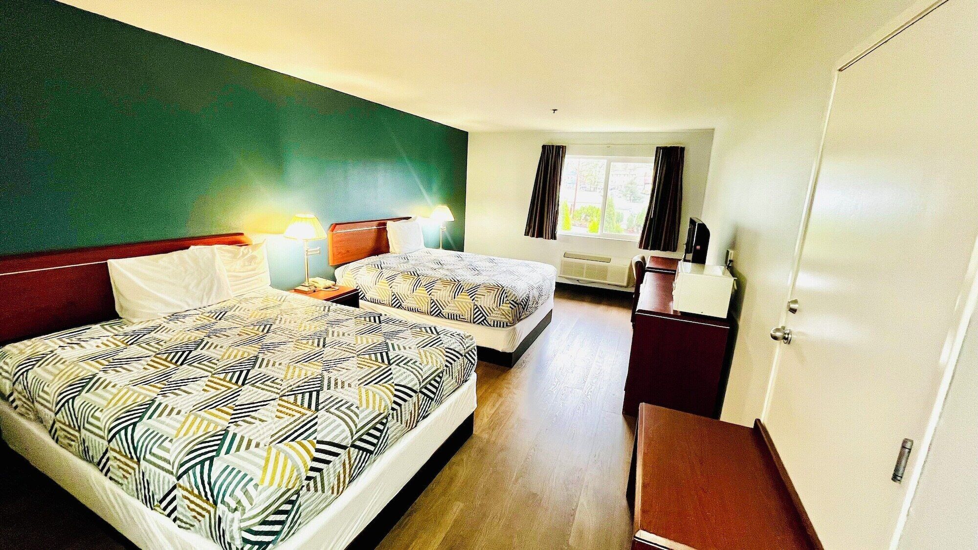 A hotel room with two beds, a desk, a chair, a mirror, and a wardrobe.