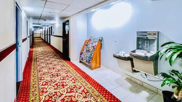 A hotel hallway with a red carpet, a reception desk, a water dispenser, and a plant.