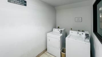 Una lavanderia con due lavatrici e asciugatrici Whirlpool, un cestino e un cartello appeso al muro.