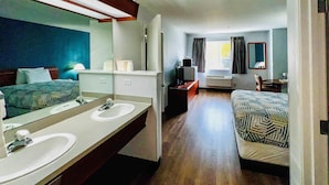 A hotel room with a large bed, a separate bathroom with a double sink, a television, and a window with curtains.