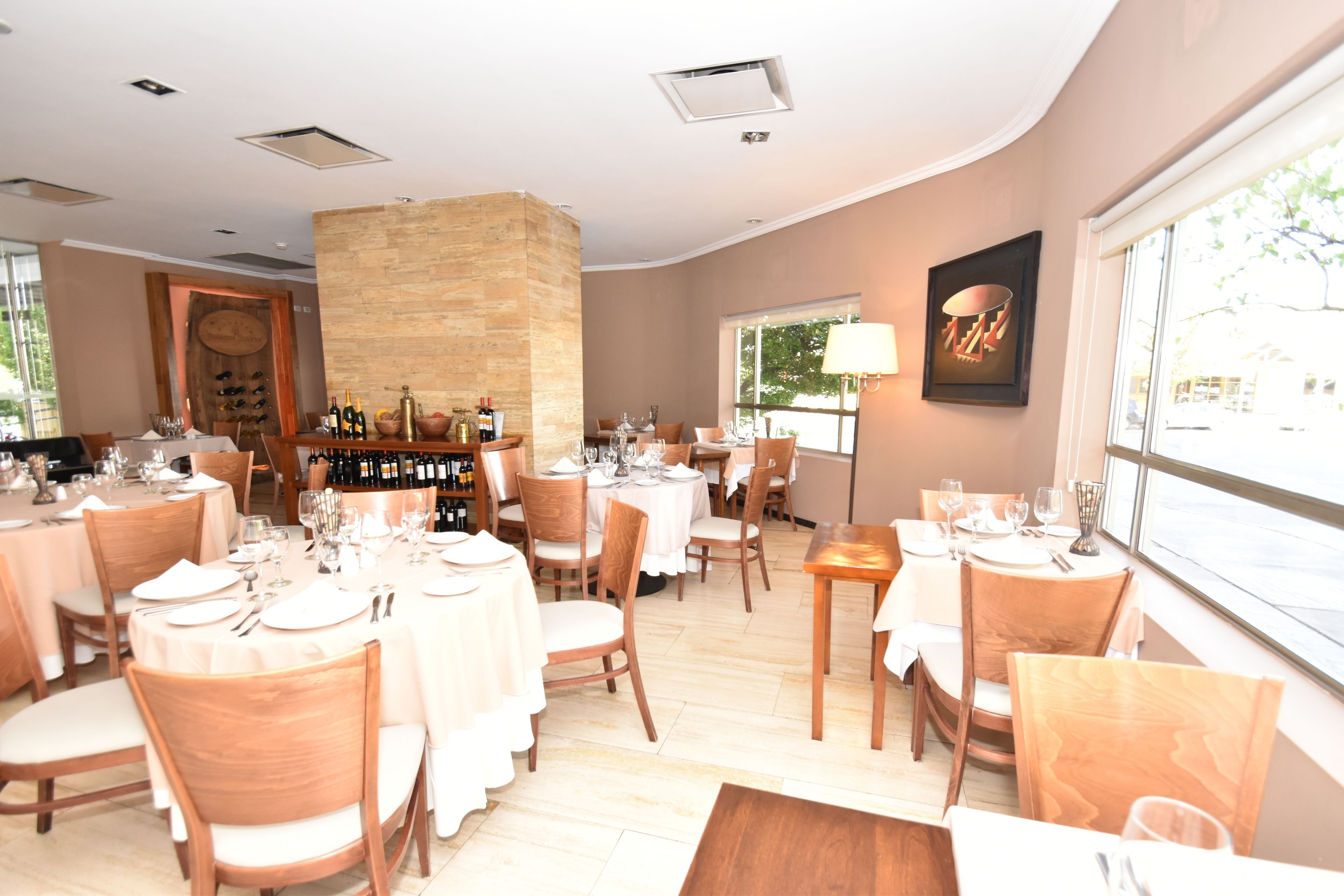 A restaurant with round tables, wooden chairs, and a stone pillar.