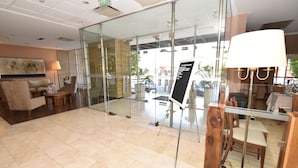 A hotel lobby with a reception desk, seating area, and a glass door leading outside.