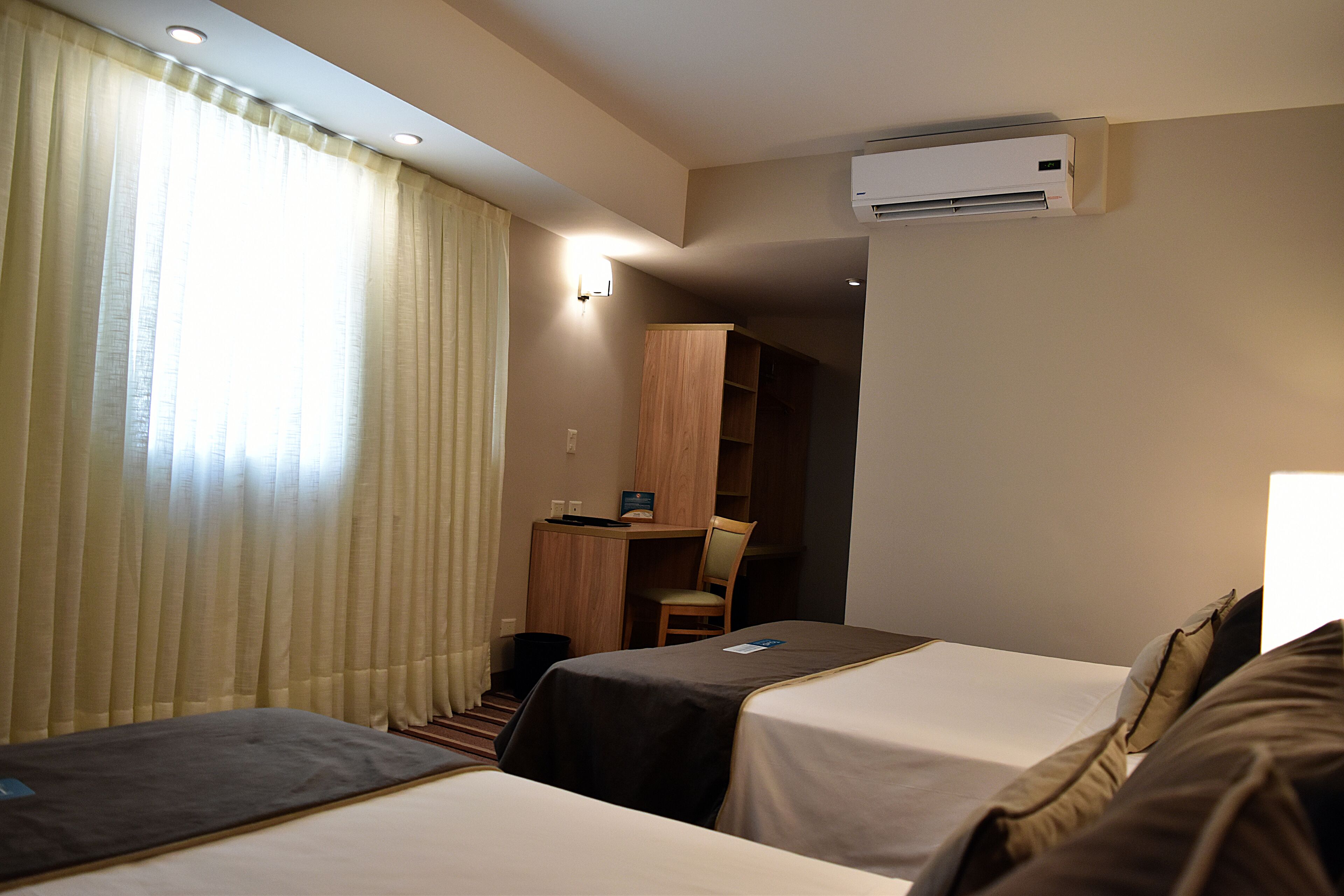 A hotel room with two beds, a desk, a chair, and an air conditioning unit.