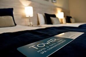 A hotel room with a bed, pillows, a nightstand, and a card indicating the hotel name and amenities.