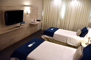 Habitación de hotel con dos camas, televisión, escritorio y ventana con cortinas.