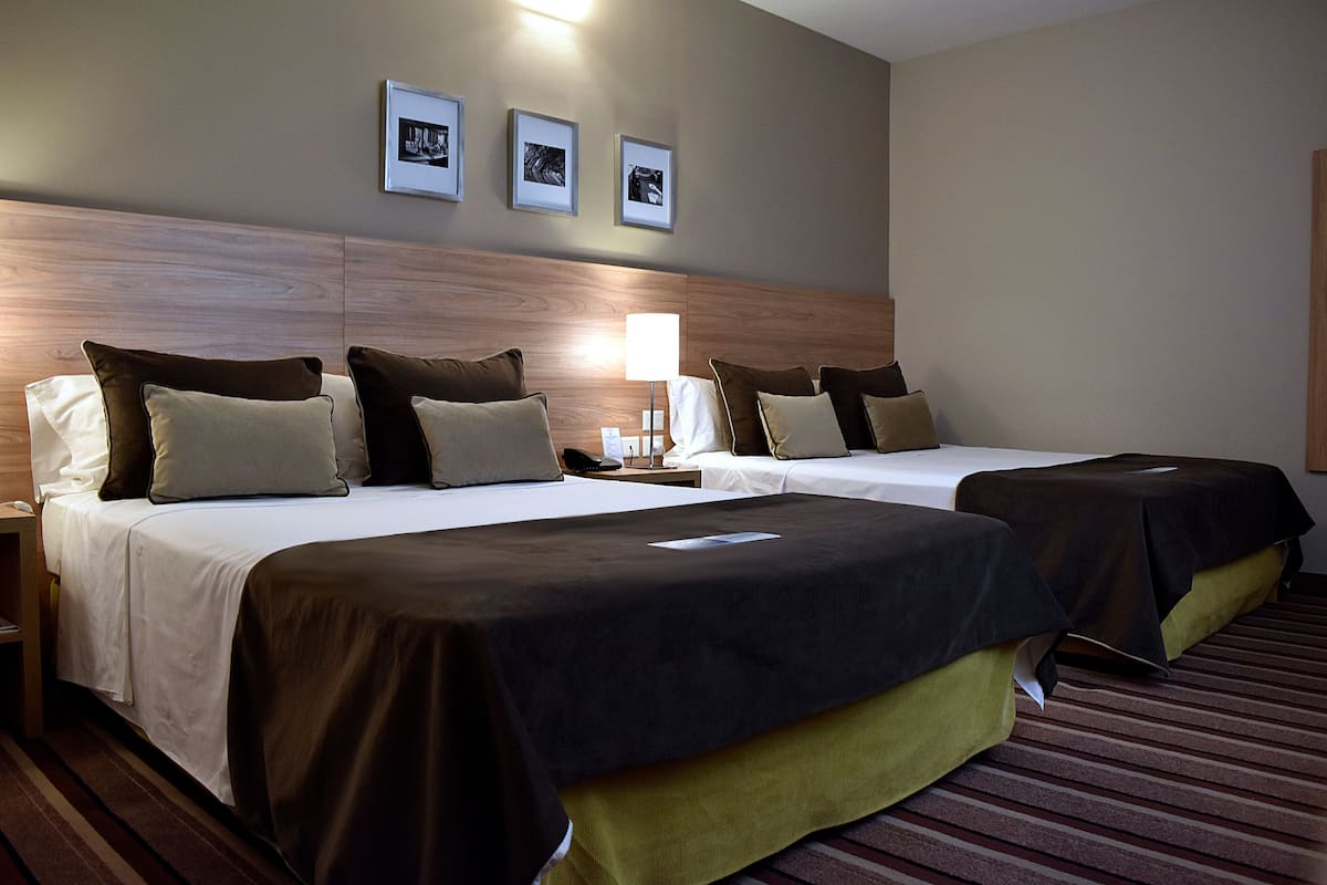 Une chambre d’hôtel avec deux lits, une table de chevet, une lampe et trois tableaux encadrés au mur.