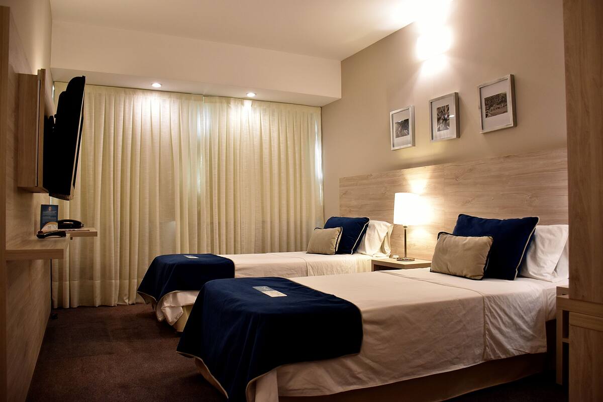 Une chambre d’hôtel avec deux lits, un bureau avec un téléphone, une lampe et un téléviseur posé sur un meuble.