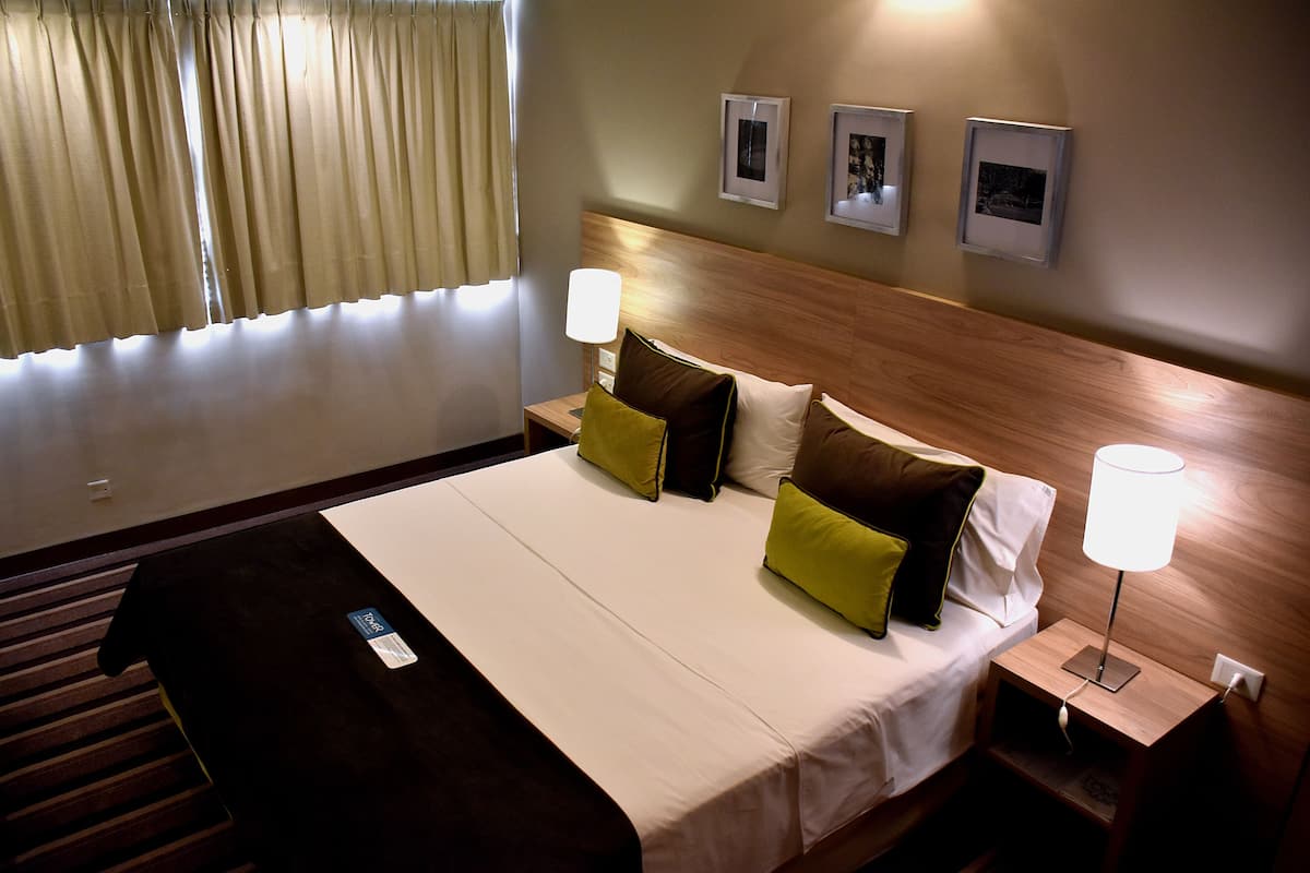 Une chambre d’hôtel avec un grand lit, deux tables de chevet et une fenêtre avec des rideaux.