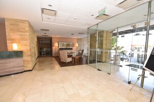 Un vestíbulo de hotel con mostrador de recepción, zona de estar y puertas de vidrio que dan al exterior.