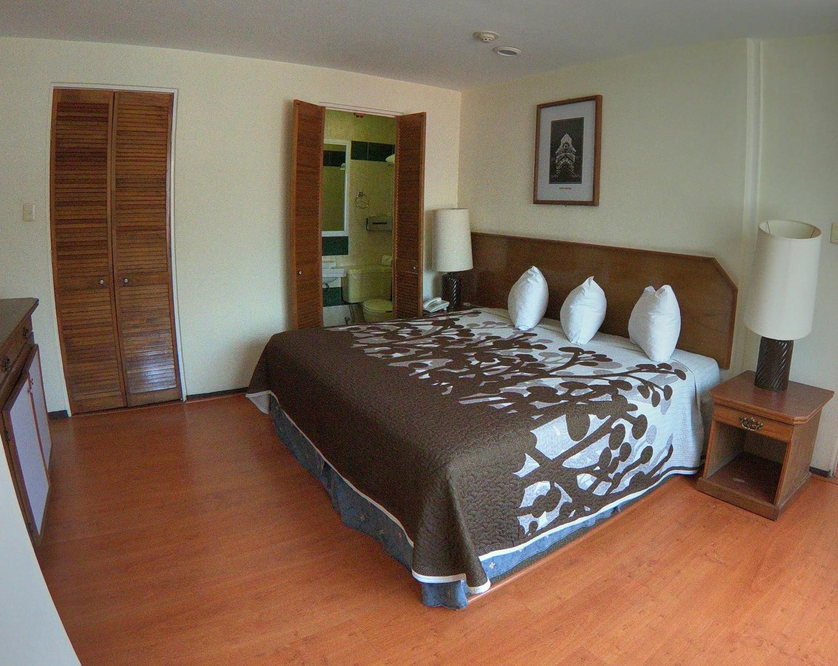 Une chambre d’hôtel avec un grand lit, une armoire en bois et une salle de bain visible à travers une porte ouverte.