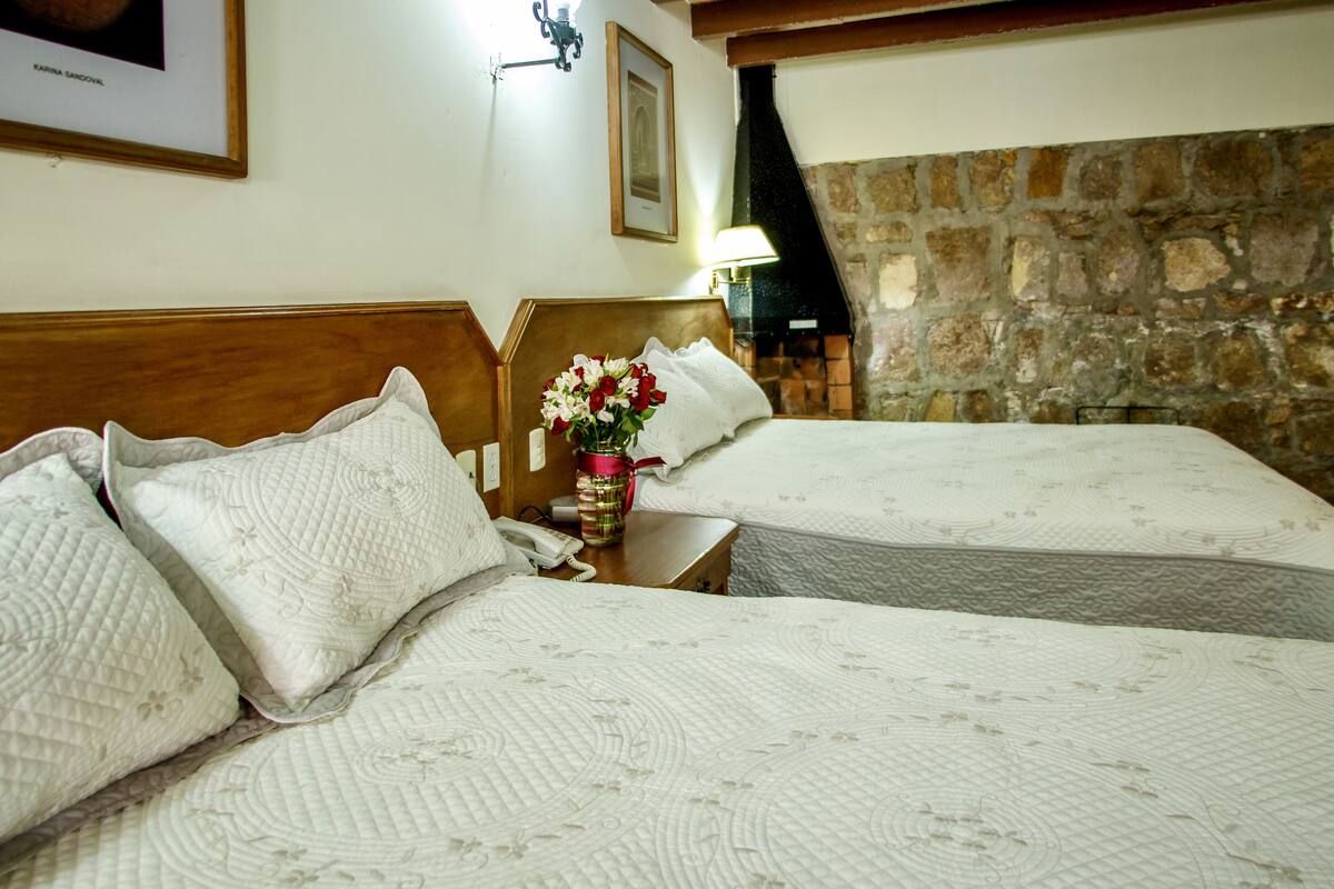 Une chambre d’hôtel avec deux lits, un mur en pierre et un tableau encadré accroché au mur.