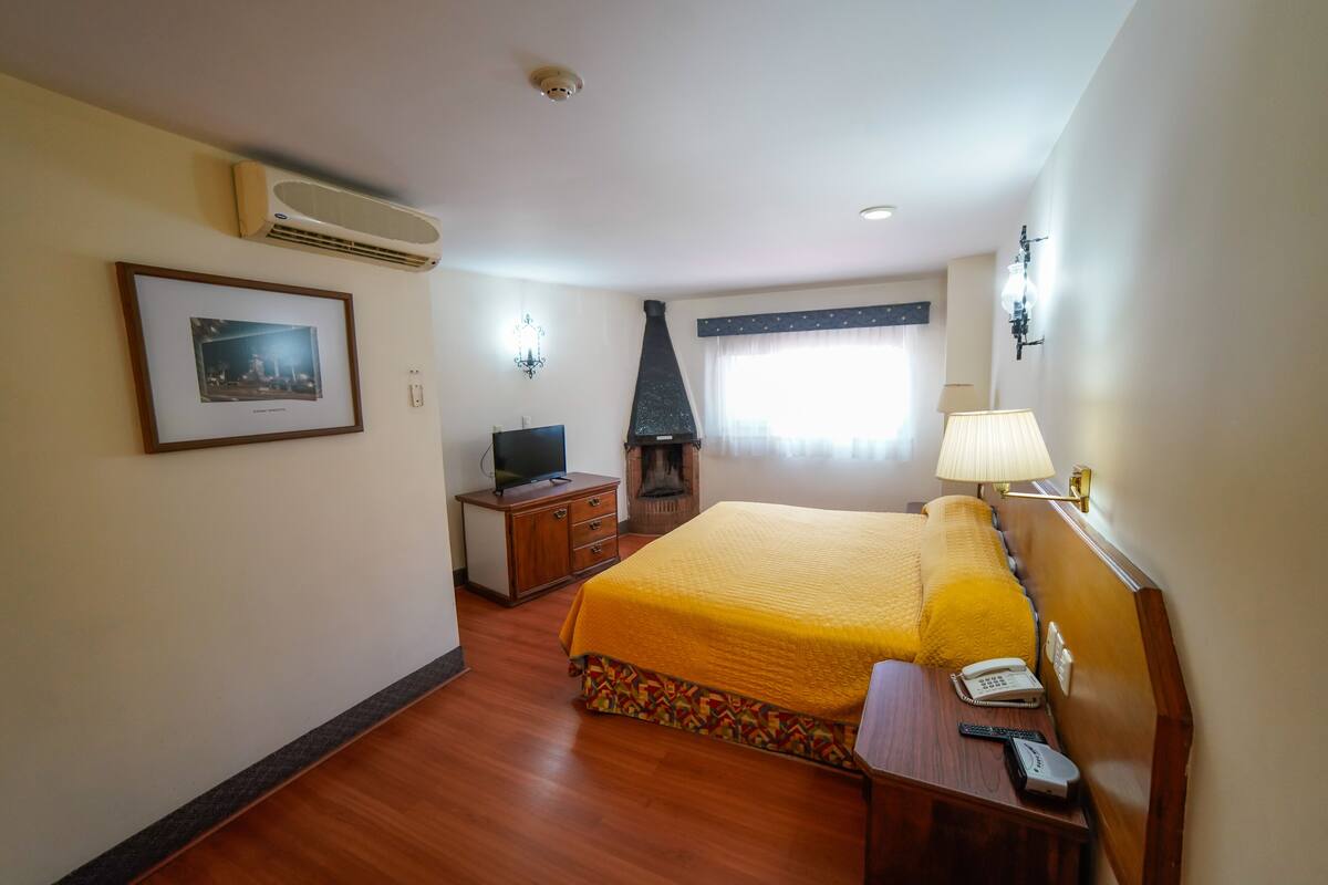 Une chambre d’hôtel avec un grand lit, un bureau avec une lampe, une télévision et une cheminée.