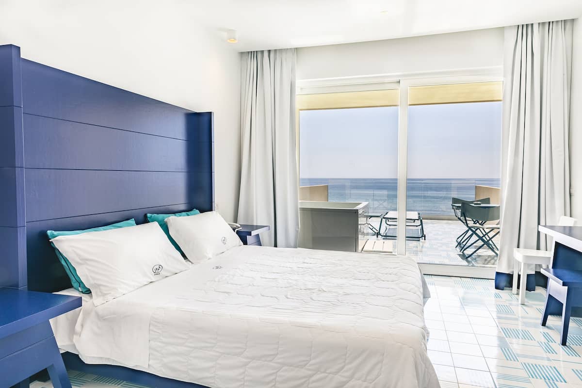 Une chambre d’hôtel avec un grand lit, un bureau et un balcon donnant sur l’océan.