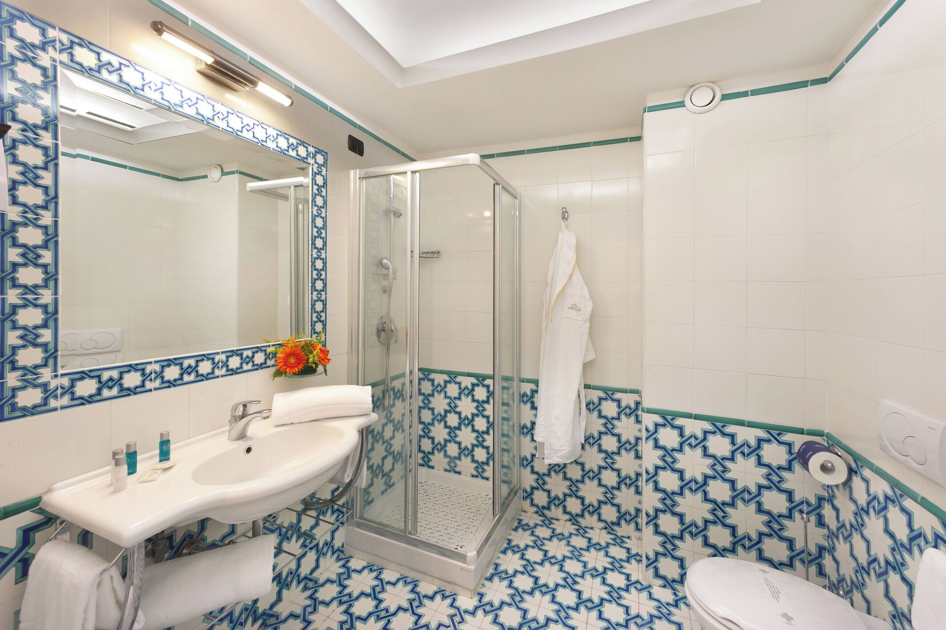 A bathroom with a glass-enclosed shower, a sink with toiletries, and a toilet.