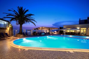 A swimming pool with lounge chairs and umbrellas, surrounded by a building with a covered area and a palm tree. - Hotel Saline Palinuro (Centola)