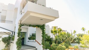 Ein modernes Gebäude mit weißer Fassade, einer überdachten Einfahrt und einem Garten mit verschiedenen Pflanzen und einem Kaktus.
