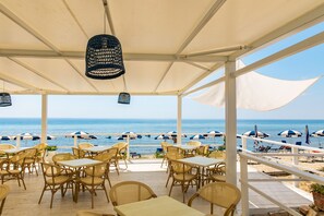 An outdoor seating area with tables and chairs, overlooking the beach and ocean. - Hotel Saline Palinuro (Centola)