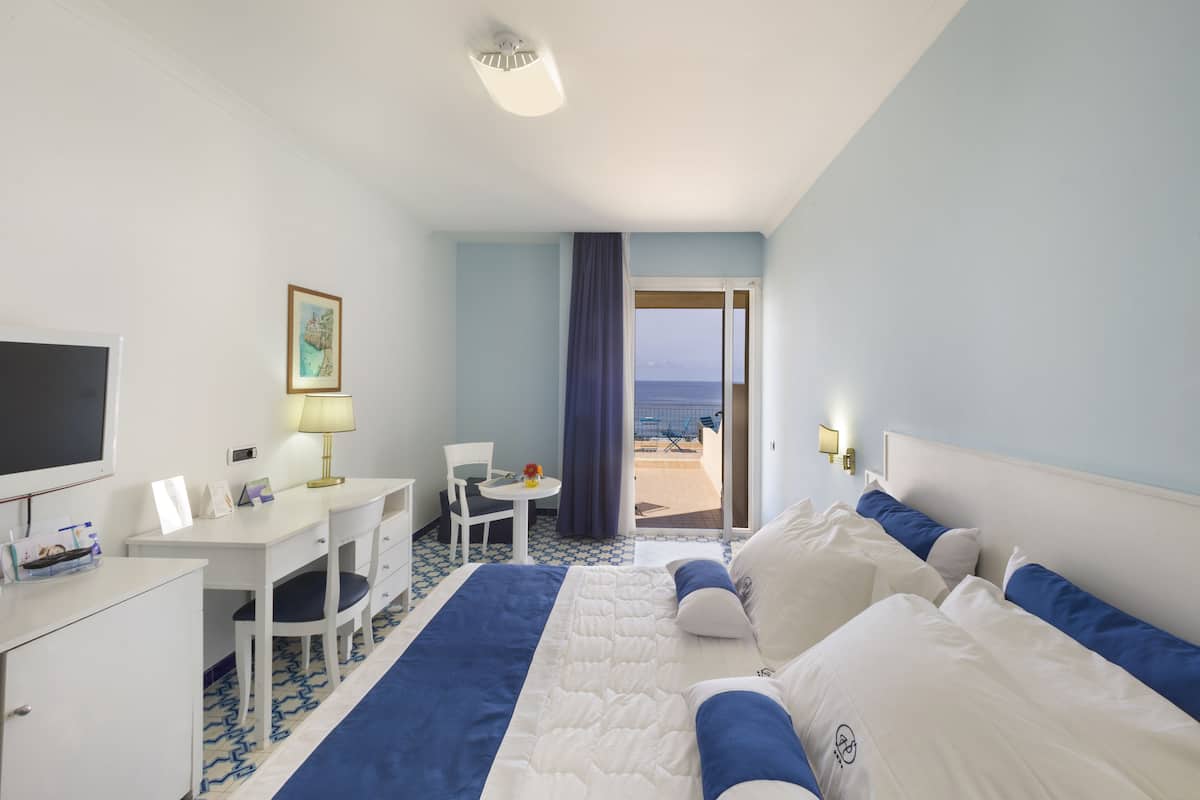 Une chambre d’hôtel avec un lit, un bureau, une chaise, une télévision et vue sur la plage.