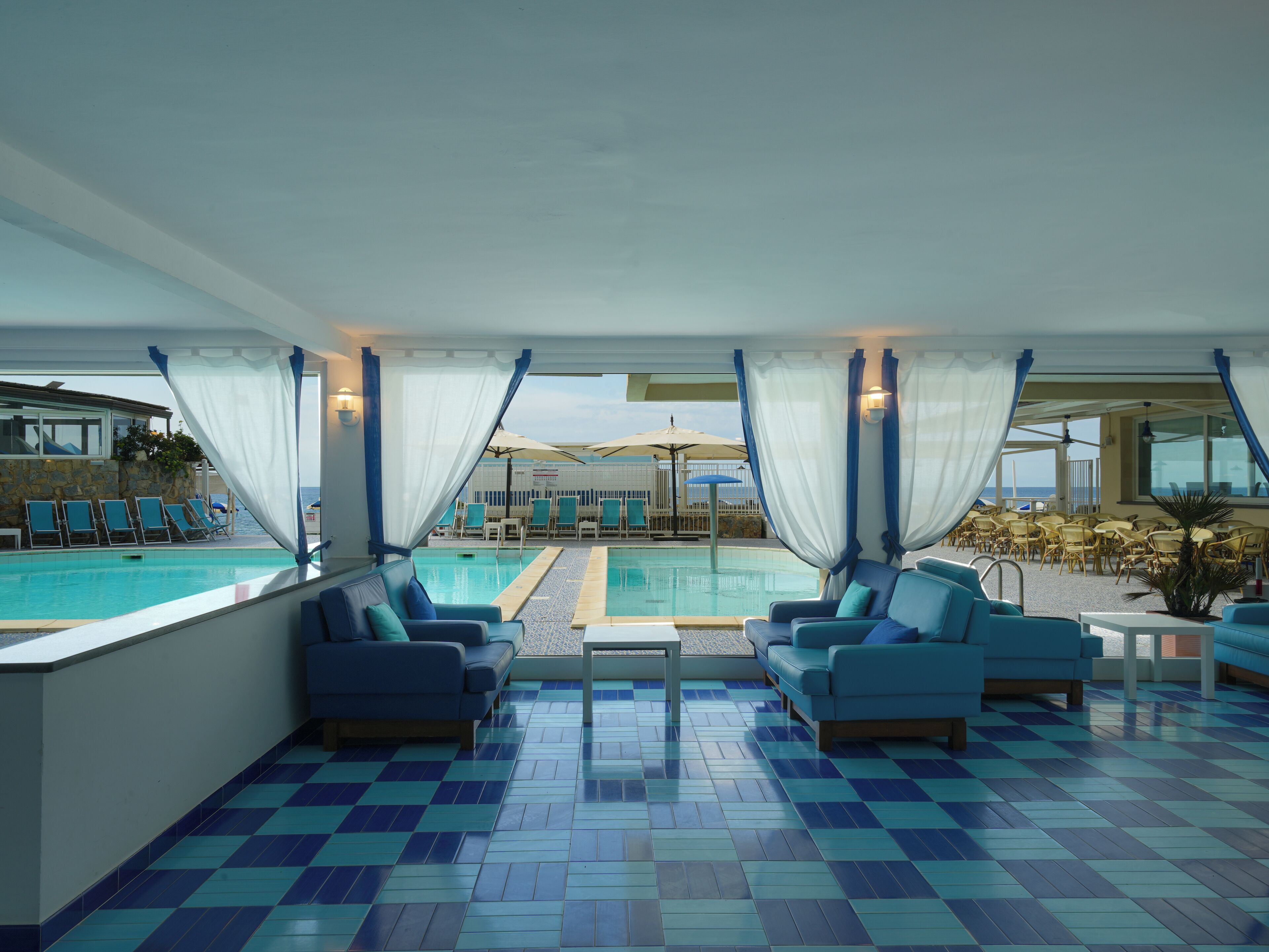 A poolside area with blue and white checkered flooring, a pool, and seating arrangements.