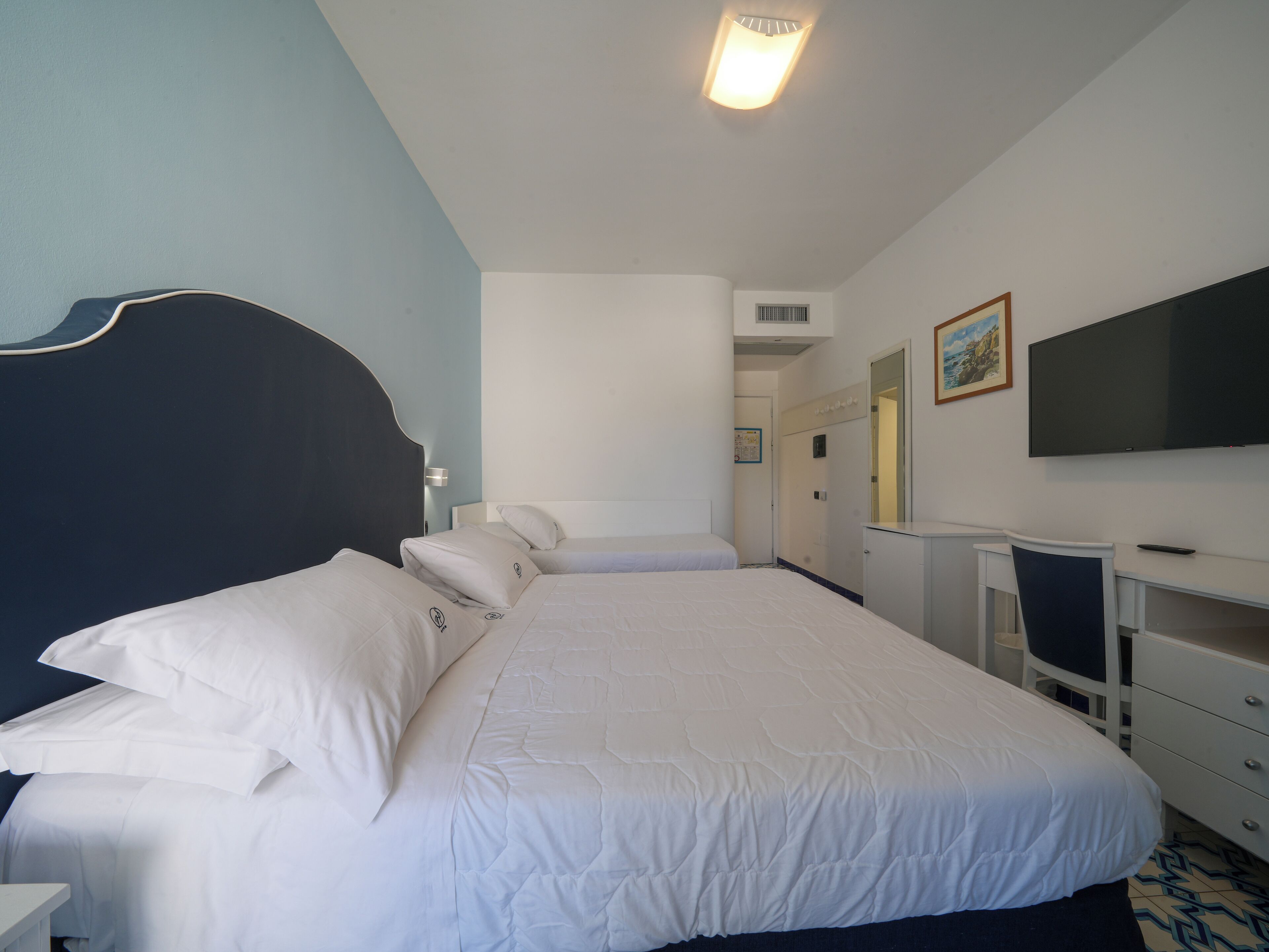 A hotel room with a large bed, a desk, a chair, a TV, and a wardrobe.
