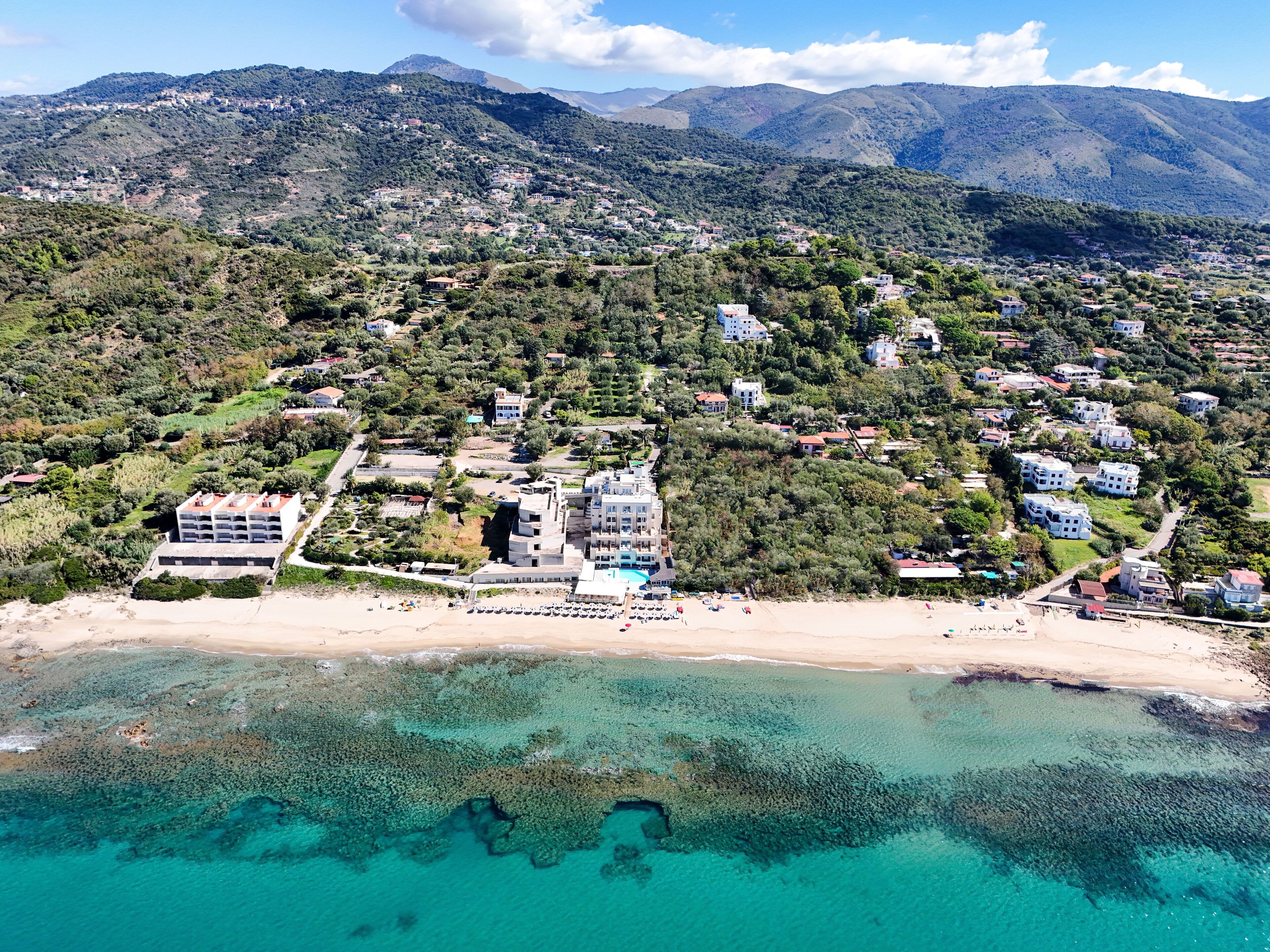 Una vista aerea di una cittadina costiera con edifici, una spiaggia e acque turchesi cristalline.