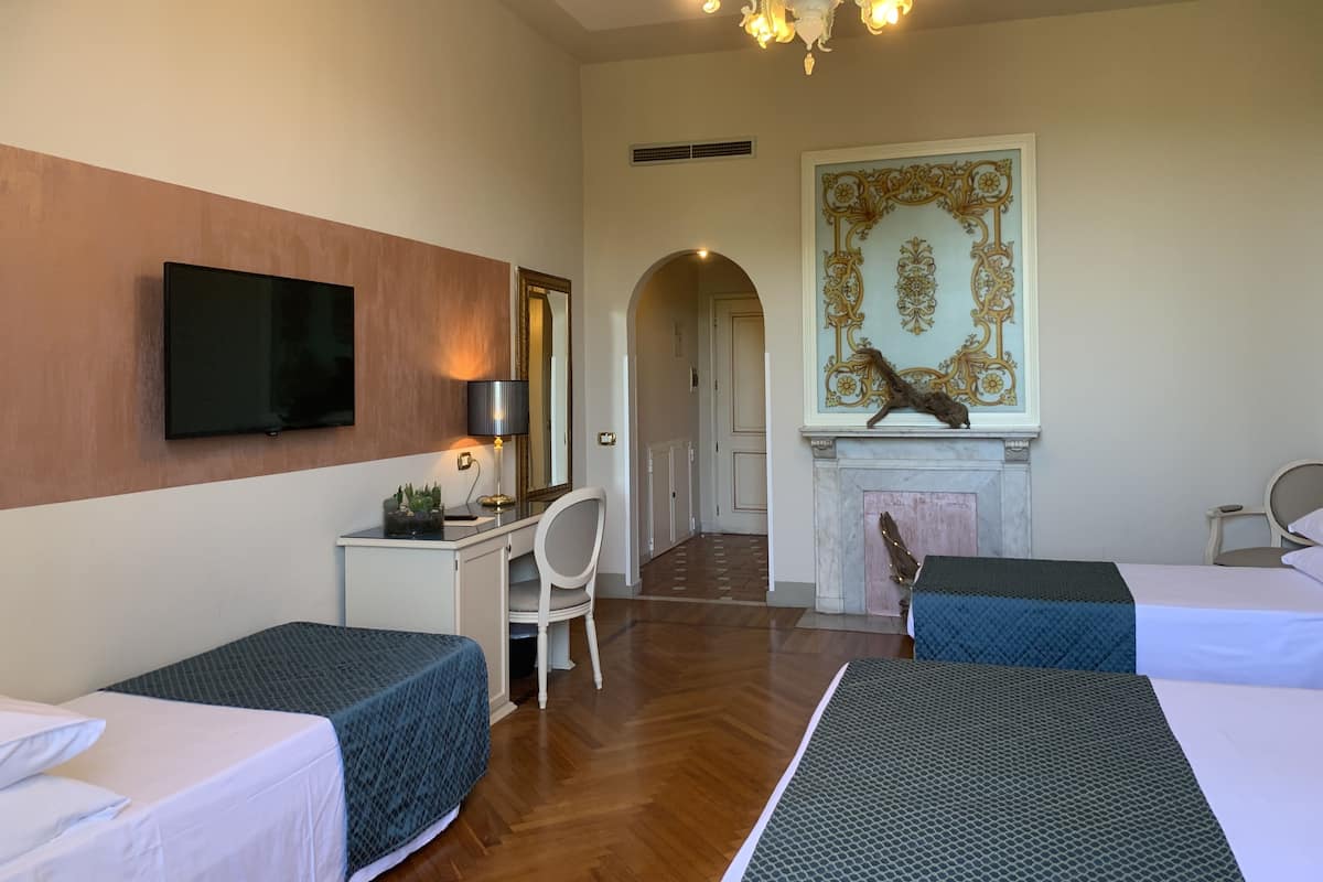 Habitación de hotel con dos camas, un escritorio con silla, televisor, candelabro y un elemento decorativo en la pared.