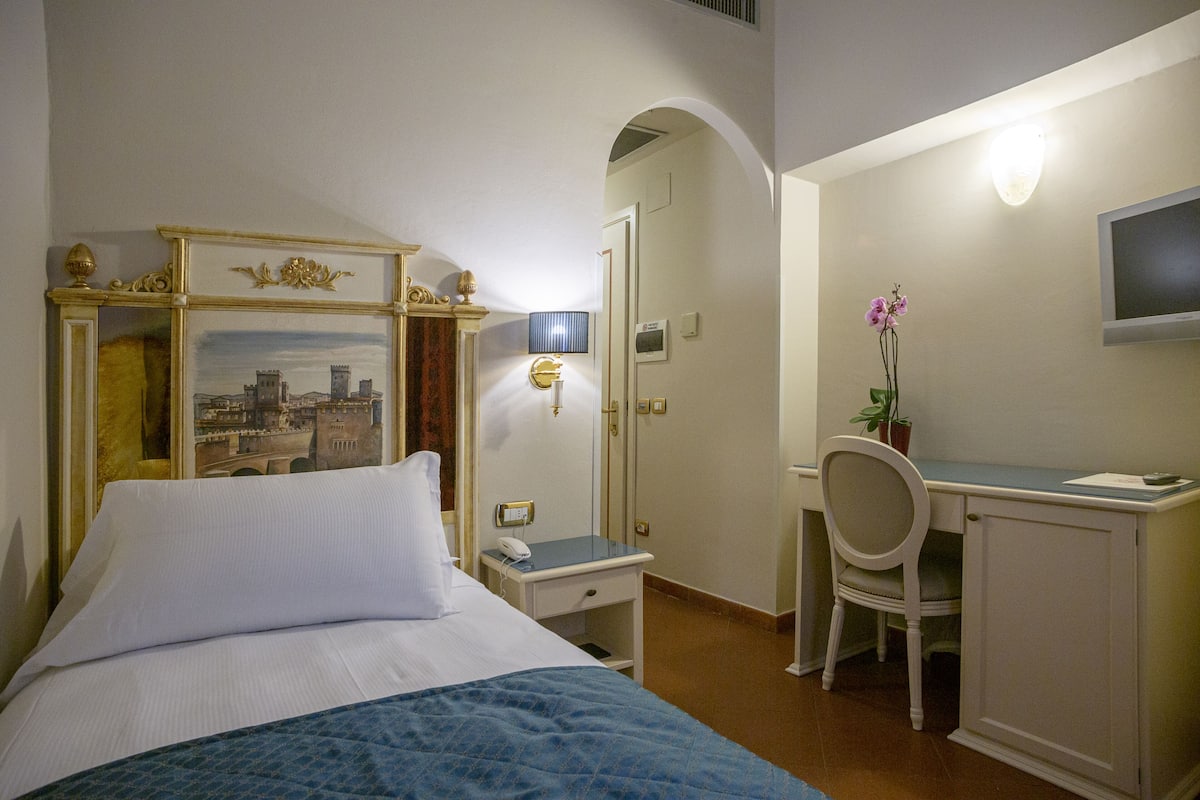 Una habitación de hotel con cama, escritorio, silla y televisión en la pared.